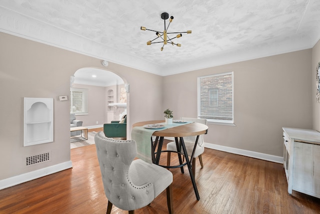 dining area with an inviting chandelier, a healthy amount of sunlight, a textured ceiling, and hardwood / wood-style flooring