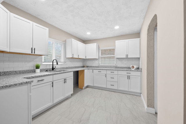 kitchen with decorative backsplash, light stone counters, a textured ceiling, sink, and white cabinets