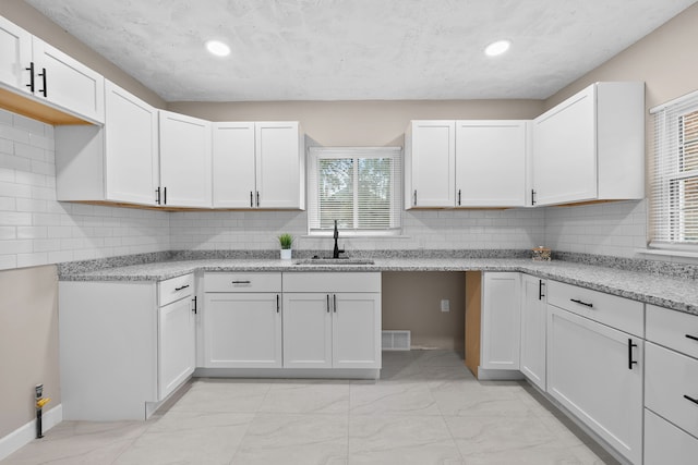 kitchen with tasteful backsplash, white cabinetry, and sink