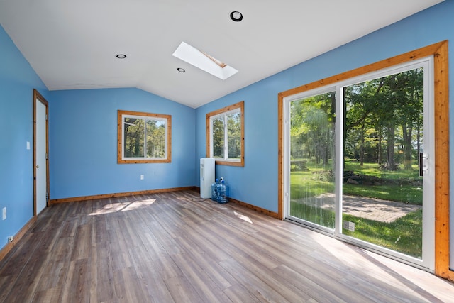 empty room with vaulted ceiling with skylight, plenty of natural light, and wood-type flooring