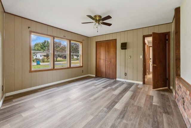 unfurnished bedroom with a closet, ceiling fan, light hardwood / wood-style flooring, and wood walls