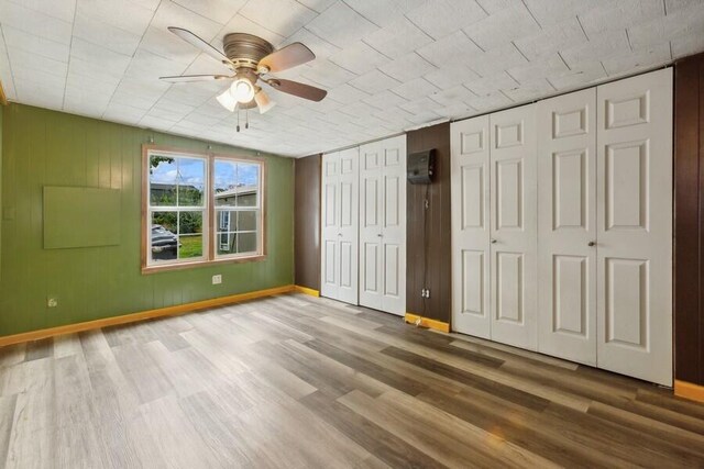 unfurnished bedroom with ceiling fan, wood-type flooring, and two closets