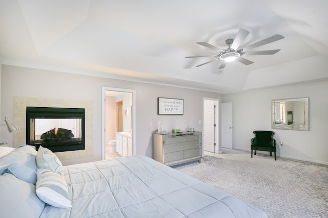 bedroom featuring light carpet, a multi sided fireplace, a raised ceiling, ensuite bath, and ceiling fan