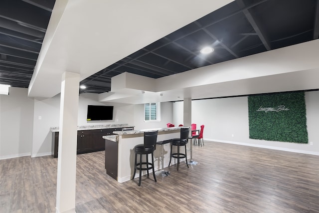 kitchen with a breakfast bar, light stone countertops, wood-type flooring, and dark brown cabinetry