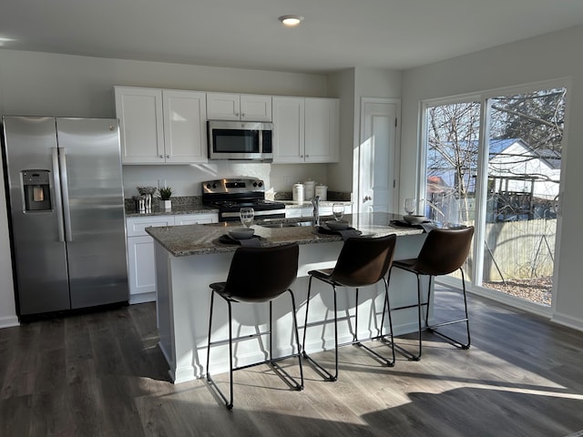 kitchen with stainless steel appliances, white cabinetry, stone countertops, and a center island with sink