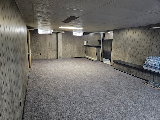 basement featuring carpet flooring, a drop ceiling, and wooden walls