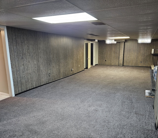 basement with carpet, a drop ceiling, and wood walls