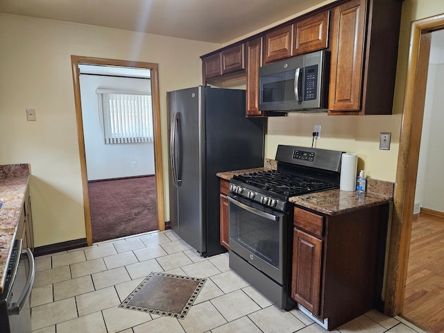 kitchen with light hardwood / wood-style floors, dark stone counters, and appliances with stainless steel finishes