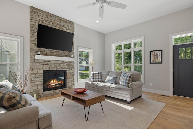 living room featuring a stone fireplace, ceiling fan, and light hardwood / wood-style floors