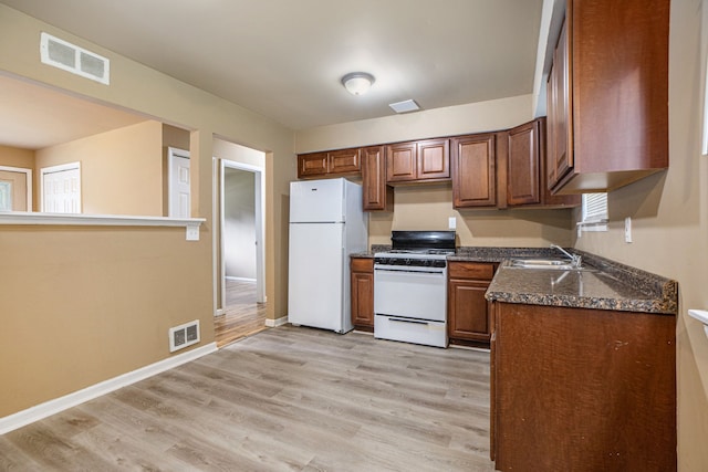 kitchen with light wood-type flooring, white appliances, dark stone counters, and sink