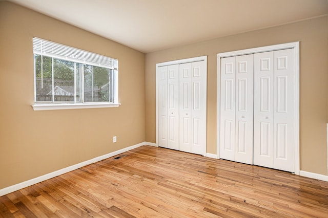 unfurnished bedroom featuring light hardwood / wood-style floors and multiple closets