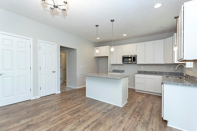 kitchen featuring stainless steel microwave, light stone counters, wood finished floors, white cabinetry, and a sink