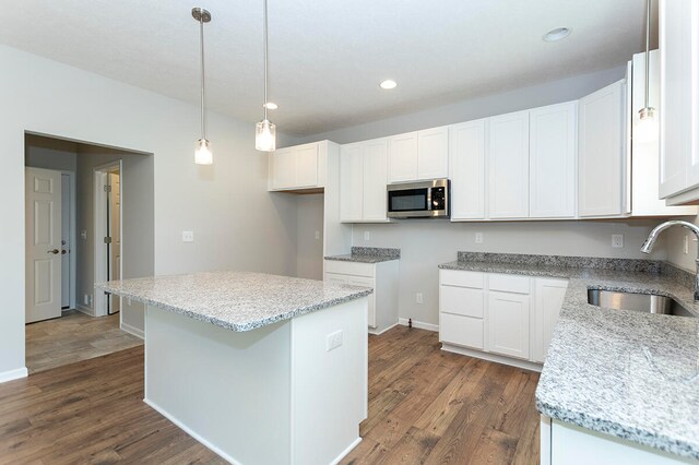 kitchen with stainless steel microwave, light stone countertops, a kitchen island, and a sink