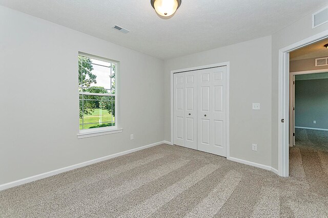 unfurnished bedroom with visible vents, a textured ceiling, a closet, carpet, and baseboards