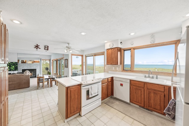 kitchen featuring a peninsula, a sink, brown cabinetry, a textured ceiling, and white appliances