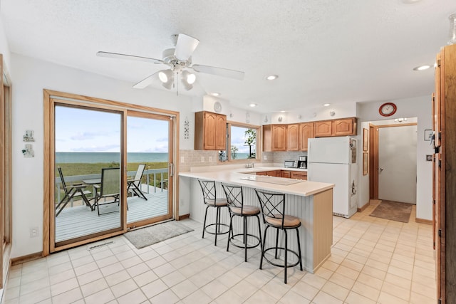 kitchen featuring a peninsula, a breakfast bar area, freestanding refrigerator, visible vents, and light countertops