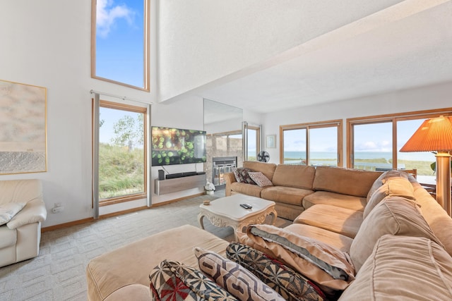 living room with a towering ceiling, light carpet, a water view, baseboards, and a tile fireplace