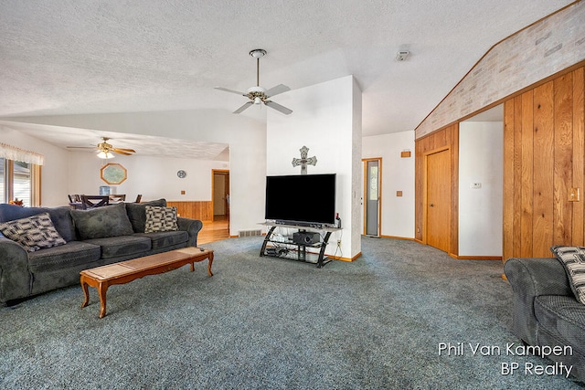 carpeted living room with a textured ceiling, wood walls, ceiling fan, and vaulted ceiling