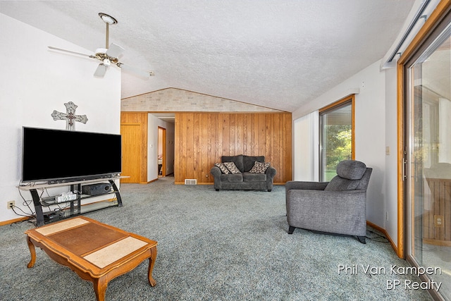 living room featuring carpet flooring, ceiling fan, wood walls, a textured ceiling, and vaulted ceiling