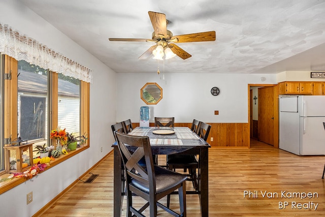 dining area featuring wooden walls, ceiling fan, and light hardwood / wood-style floors