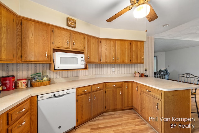 kitchen with a breakfast bar, white appliances, light hardwood / wood-style flooring, ceiling fan, and kitchen peninsula