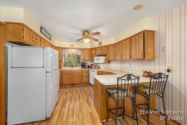 kitchen with white appliances, sink, light wood-type flooring, kitchen peninsula, and a breakfast bar area