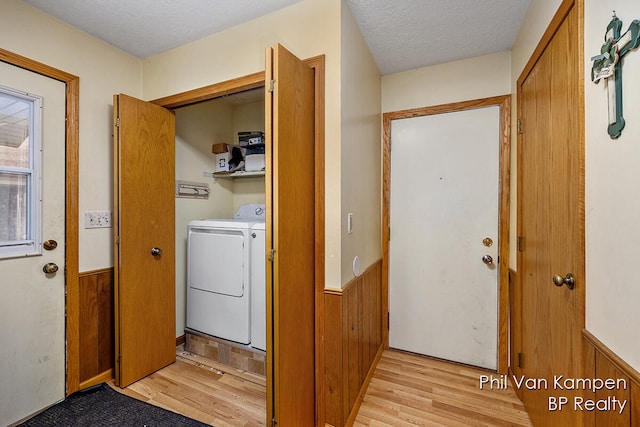 laundry area featuring a textured ceiling, light wood-type flooring, washer and clothes dryer, and wood walls