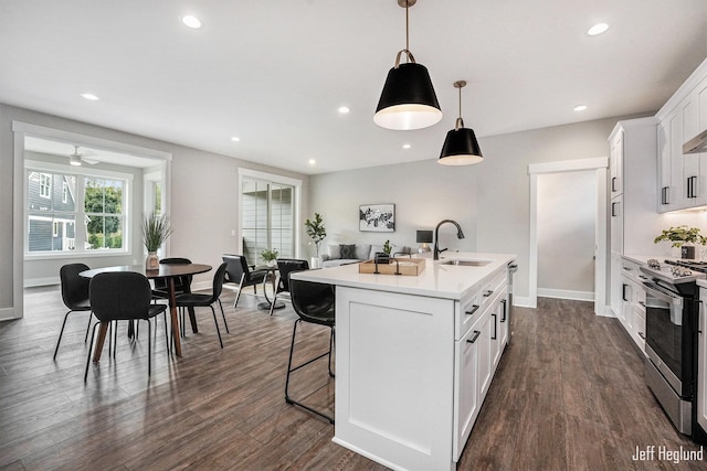 kitchen featuring white cabinetry, sink, hanging light fixtures, an island with sink, and stainless steel stove