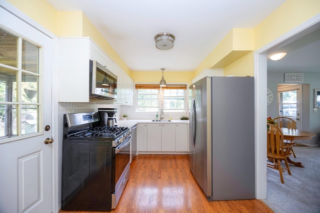 kitchen featuring stainless steel appliances, sink, white cabinets, hardwood / wood-style floors, and hanging light fixtures