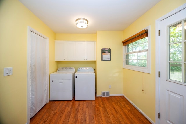 laundry room with washing machine and dryer, a healthy amount of sunlight, hardwood / wood-style floors, and cabinets