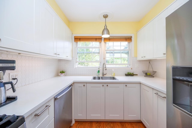 kitchen with white cabinetry, sink, hanging light fixtures, stainless steel appliances, and light wood-type flooring