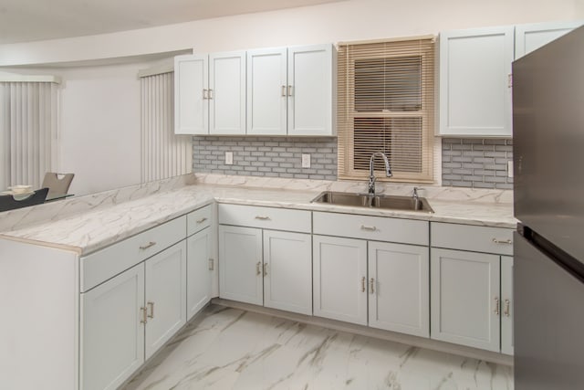 kitchen with decorative backsplash, stainless steel fridge, sink, and light stone countertops