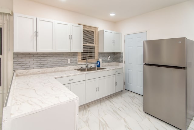 kitchen featuring white cabinets, decorative backsplash, sink, and stainless steel refrigerator