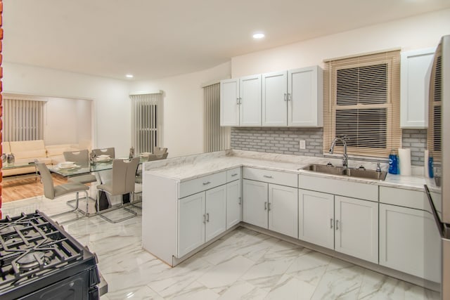 kitchen with backsplash, kitchen peninsula, sink, light stone countertops, and white cabinetry