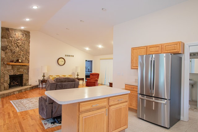 kitchen with stainless steel fridge, lofted ceiling, a fireplace, a kitchen island, and light wood-type flooring