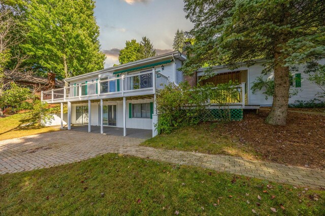 back house at dusk with a patio, a wooden deck, and a lawn