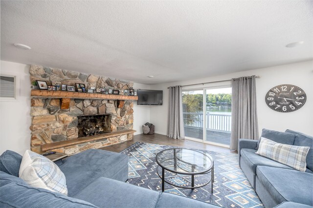 living room with a textured ceiling, hardwood / wood-style flooring, and a stone fireplace