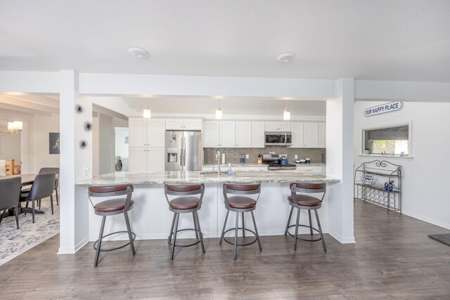 kitchen featuring dark wood-type flooring, a kitchen breakfast bar, appliances with stainless steel finishes, white cabinetry, and kitchen peninsula