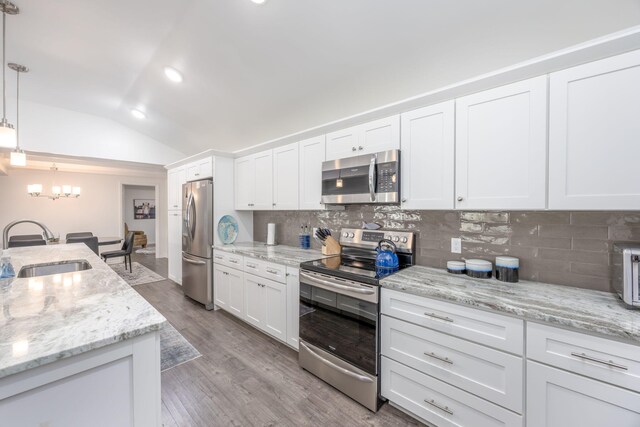 kitchen featuring stainless steel appliances, vaulted ceiling, sink, white cabinetry, and hanging light fixtures