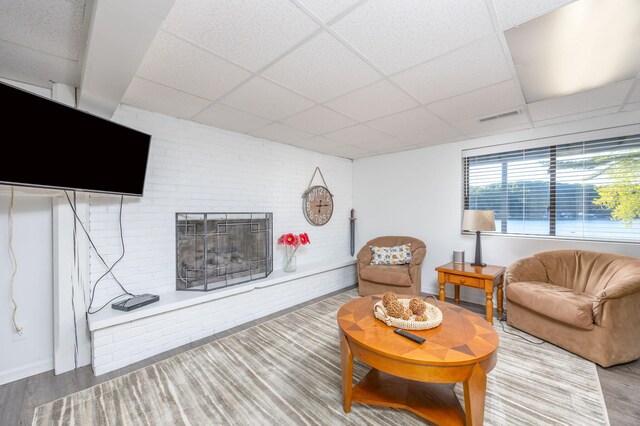 living room featuring hardwood / wood-style flooring, a drop ceiling, and a brick fireplace