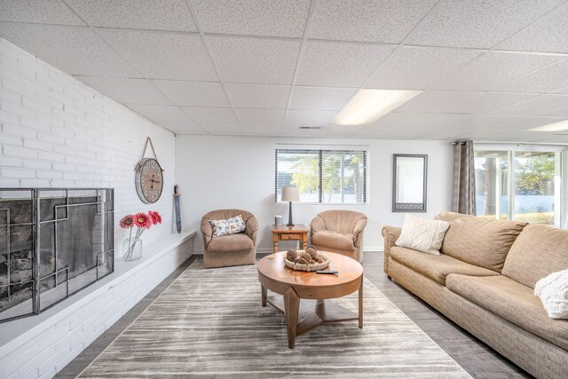 living room featuring a fireplace, hardwood / wood-style flooring, a drop ceiling, and brick wall