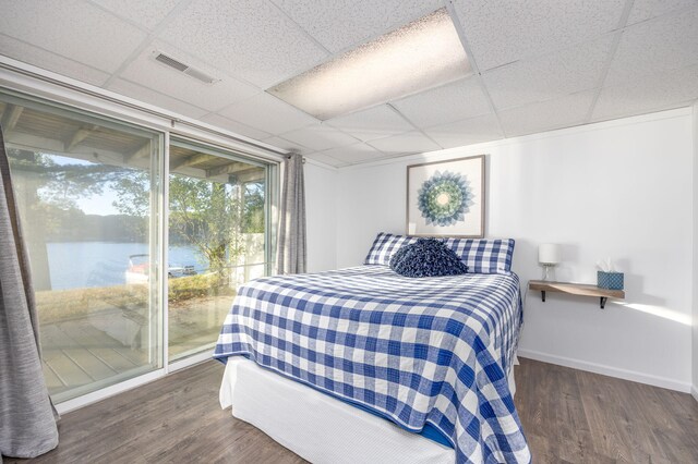 bedroom featuring access to exterior, a paneled ceiling, a water view, and dark wood-type flooring