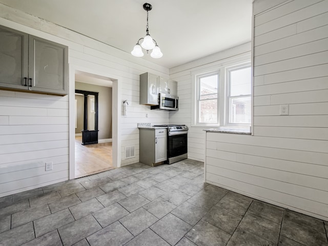 kitchen with appliances with stainless steel finishes, pendant lighting, gray cabinetry, and wood walls