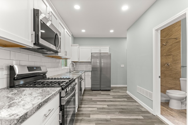 kitchen with white cabinetry, sink, stainless steel appliances, light stone counters, and light wood-type flooring