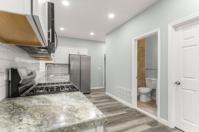 kitchen with white cabinetry, sink, light stone counters, light hardwood / wood-style flooring, and appliances with stainless steel finishes