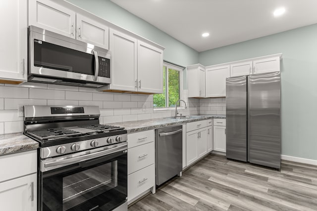 kitchen featuring white cabinets, appliances with stainless steel finishes, light wood-type flooring, and light stone countertops