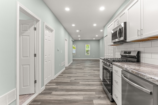 kitchen with backsplash, light wood-type flooring, light stone counters, white cabinetry, and stainless steel appliances