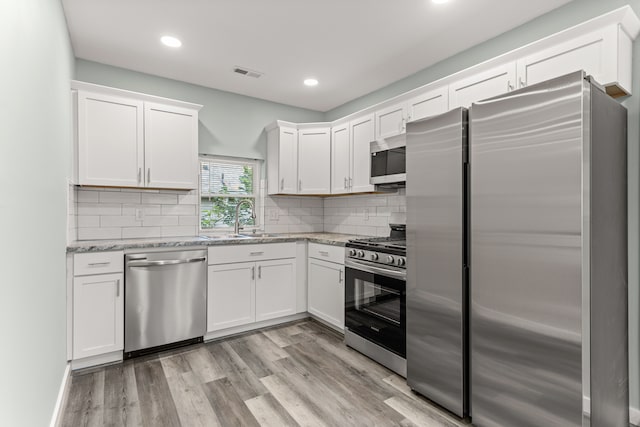 kitchen featuring light stone countertops, stainless steel appliances, sink, light hardwood / wood-style flooring, and white cabinetry