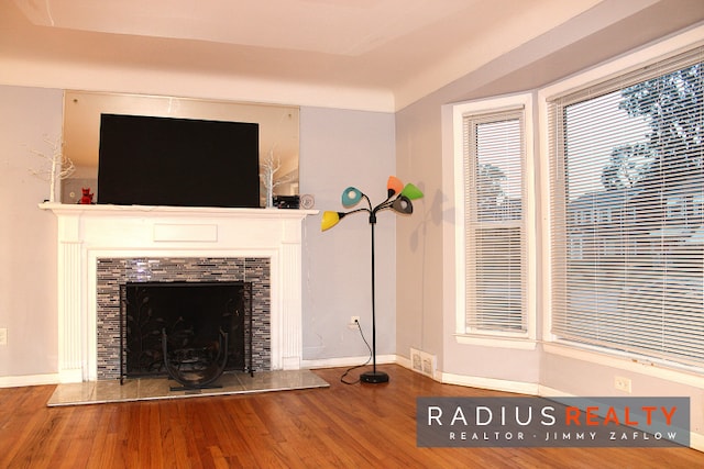 unfurnished living room featuring a tiled fireplace, wood-type flooring, and vaulted ceiling