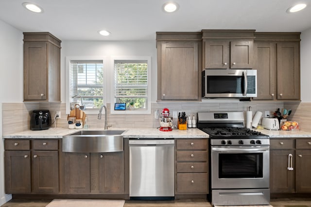 kitchen featuring appliances with stainless steel finishes, backsplash, light stone counters, sink, and light hardwood / wood-style flooring